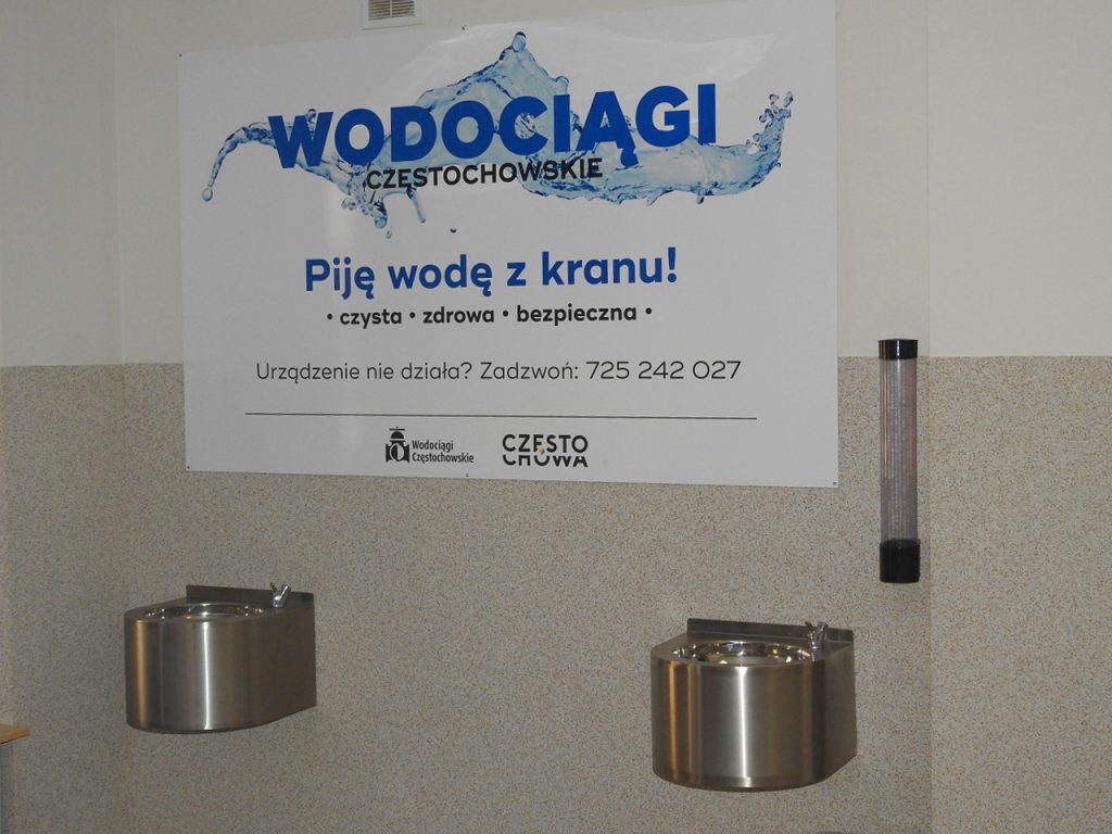 Tablica częstochowskich Wodociągów, na której widnieje napis: ,,Piję wodę  z kranu czysta, zdrowa, bezpieczna. Urządzenie nie działa zadzwoń 725 242 027''.