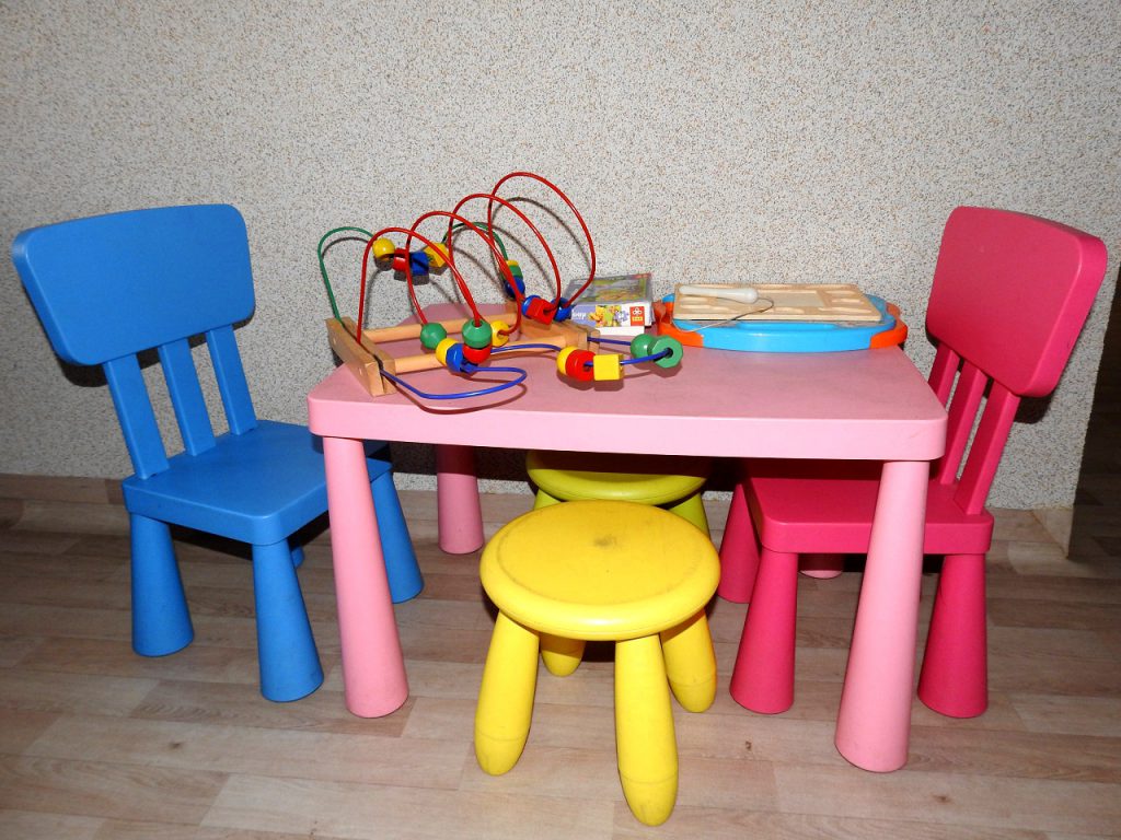 Kącik zabaw dla dzieci, w którym znajdują się plastikowe krzesełka, stolik oraz kilka zabawek.